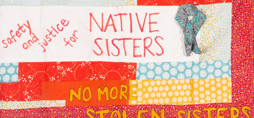 A closeup of a quilt piece with text, including the words "No More Stolen Sisters" 