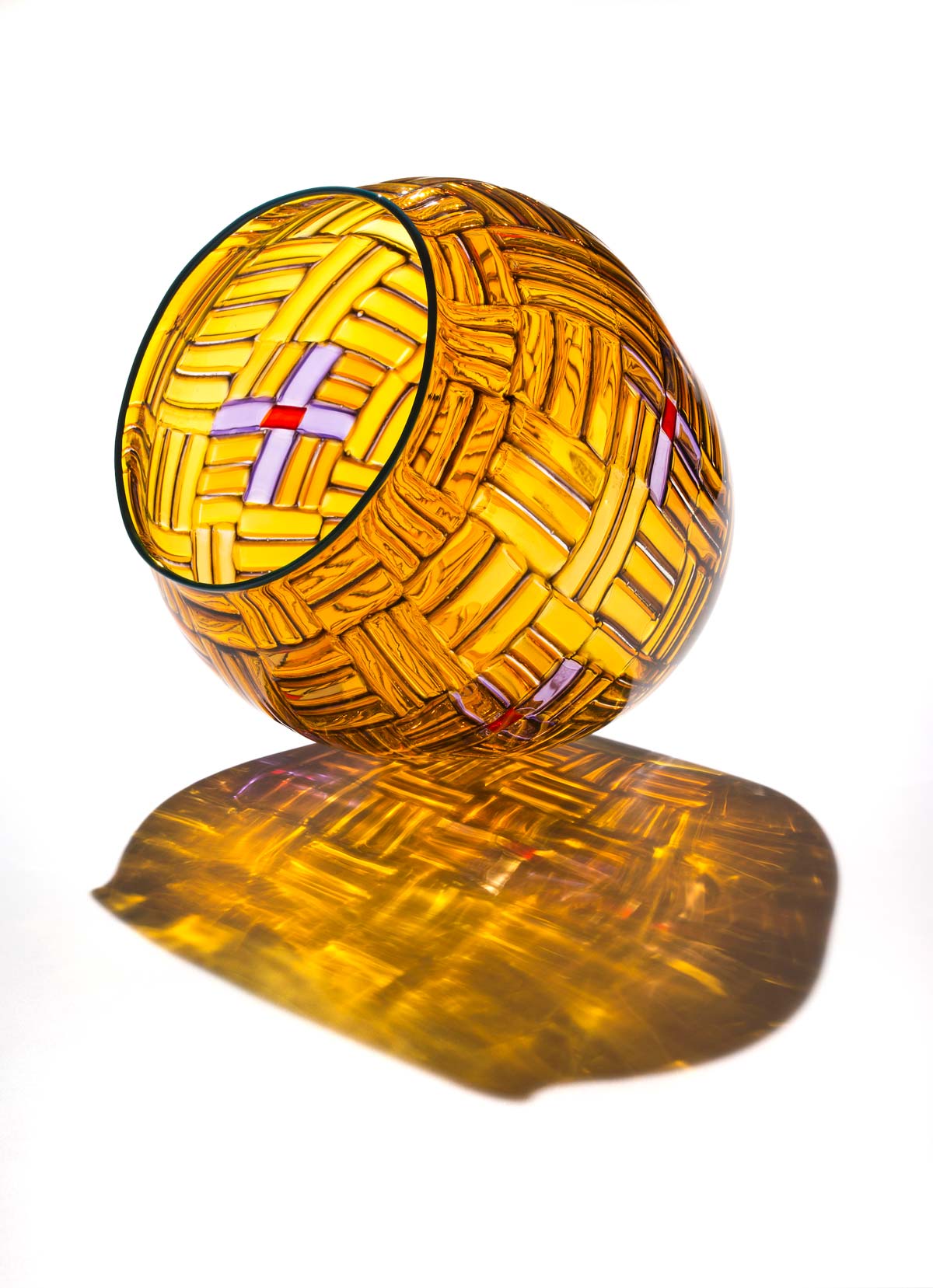 A golden glass pot tilted on pot tilts on its side, illuminating a golden shadow from the light reflected through the glass.