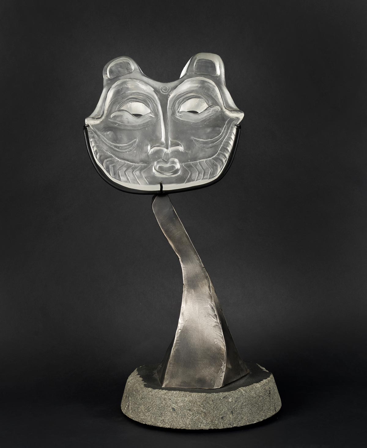 Silver crystal and steel sculpture of mask perched on a silver pedestal 