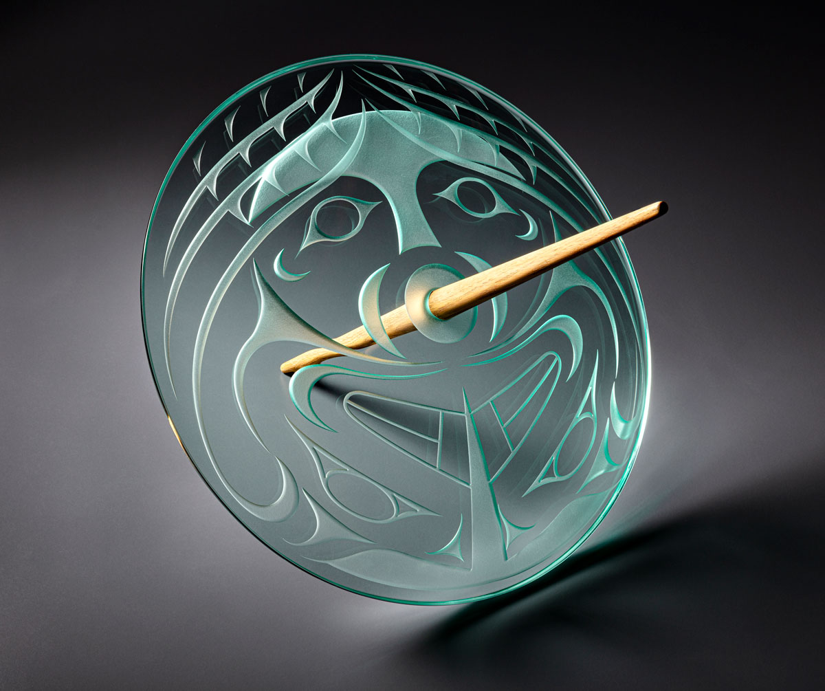 A multimedia clear glass sculpture with the etchings of a face, punctured by maple spindle.