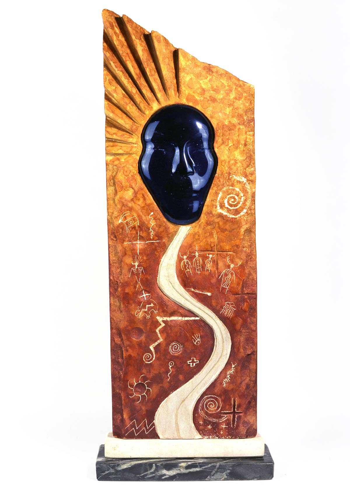 An abstract red and orange glass and limestone sculpture depicting several etchings and a pathway leading to a radiating face.