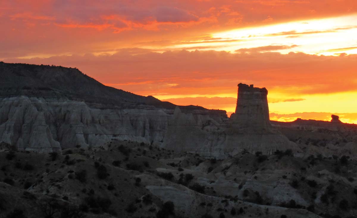 Red and yellow sunset scene with silhouetted mesa and desert landscape.