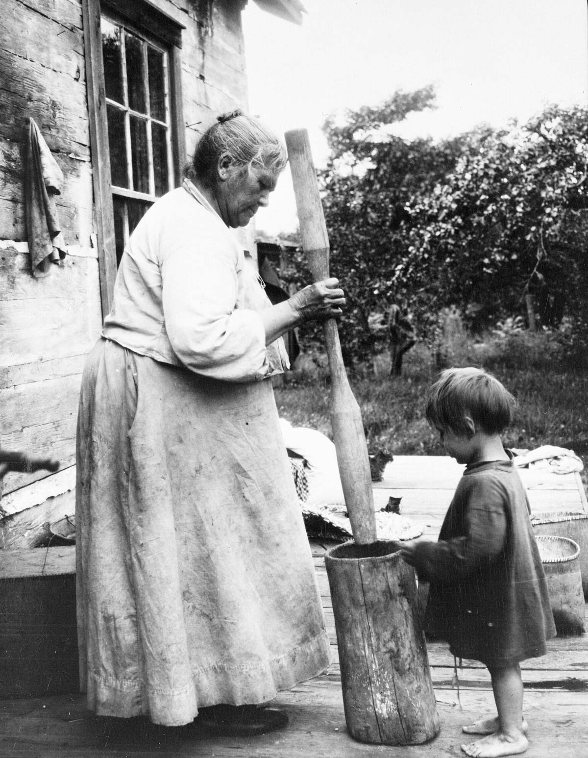 Grandmother and child working with a large mortar and pestle.