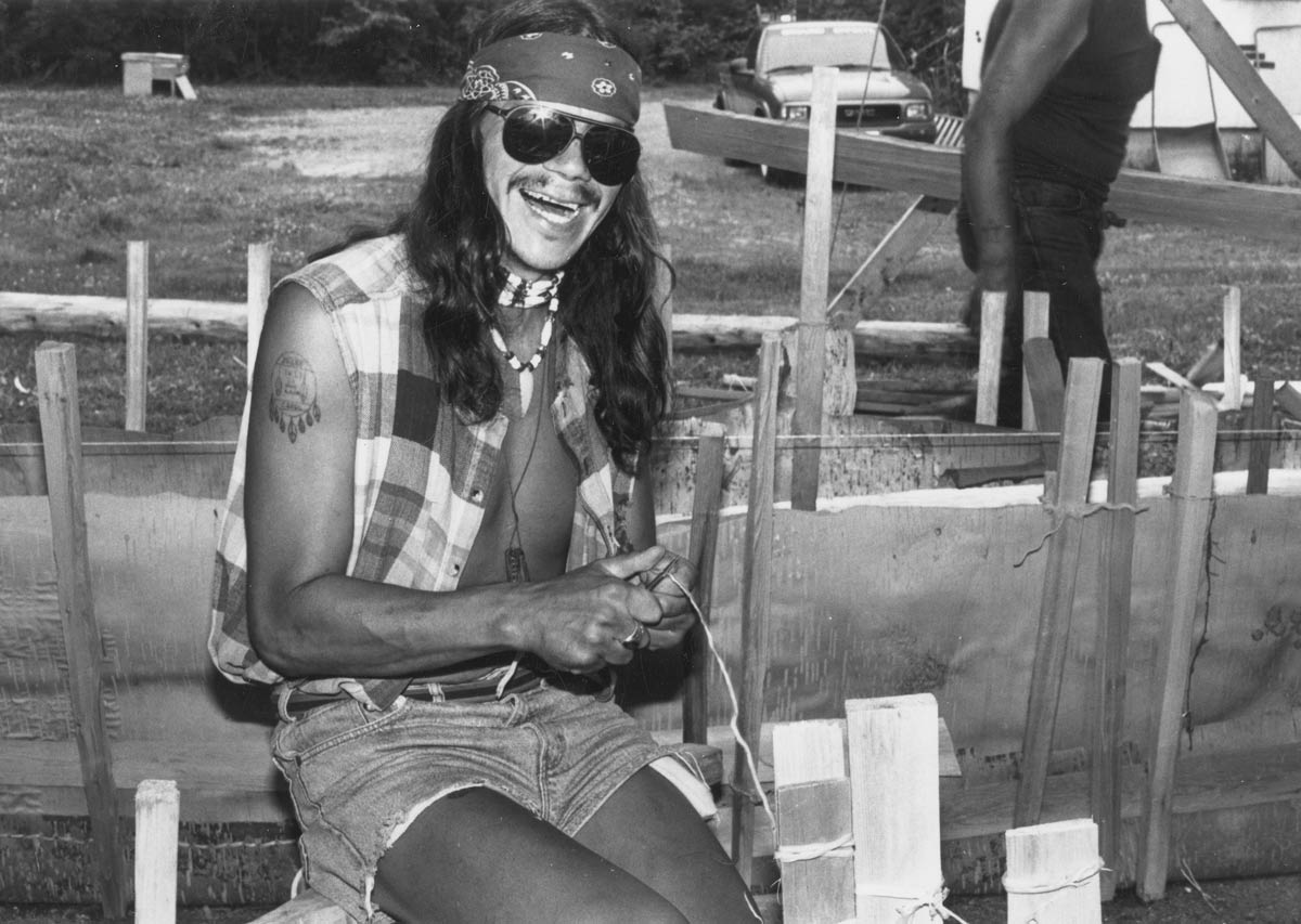 Person using knife to split roots wearing demin shorts and flannel shirt.
