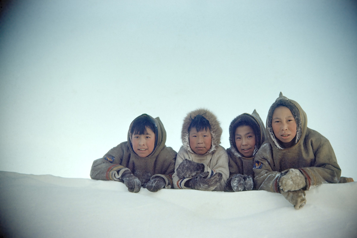 A group of four boys in parkas and gloves lay on a snowbank.