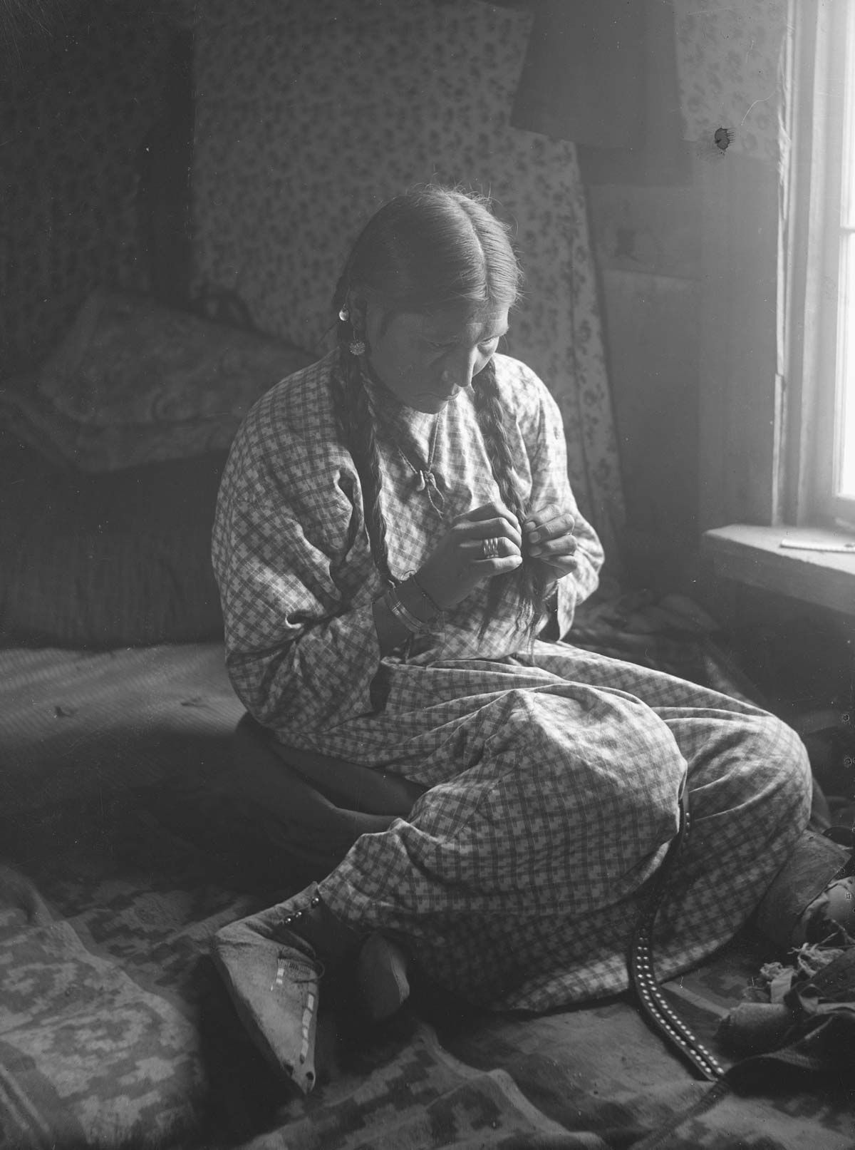 A woman in a long dress sits on the floor and braids her hair.