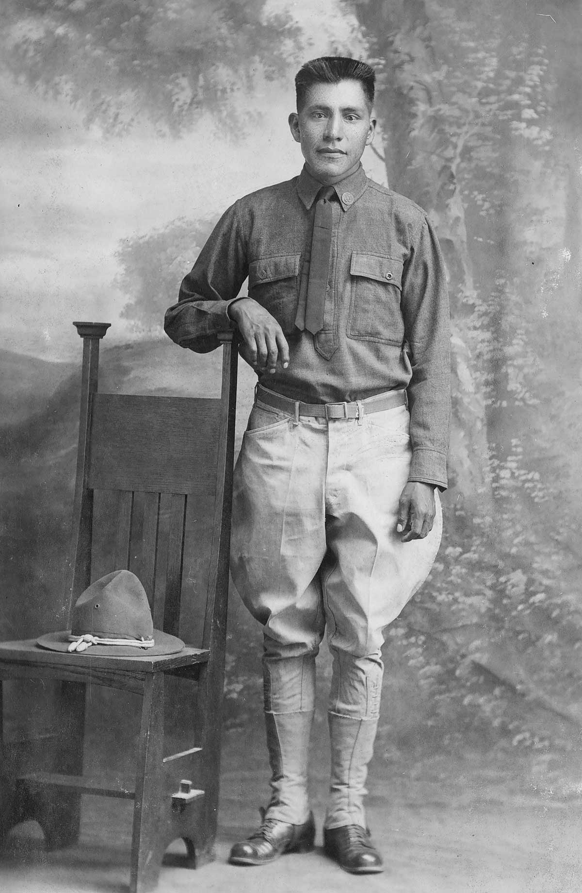 Musician Fist Class Guy Maktima stands in military uniform with his arm on a chair.