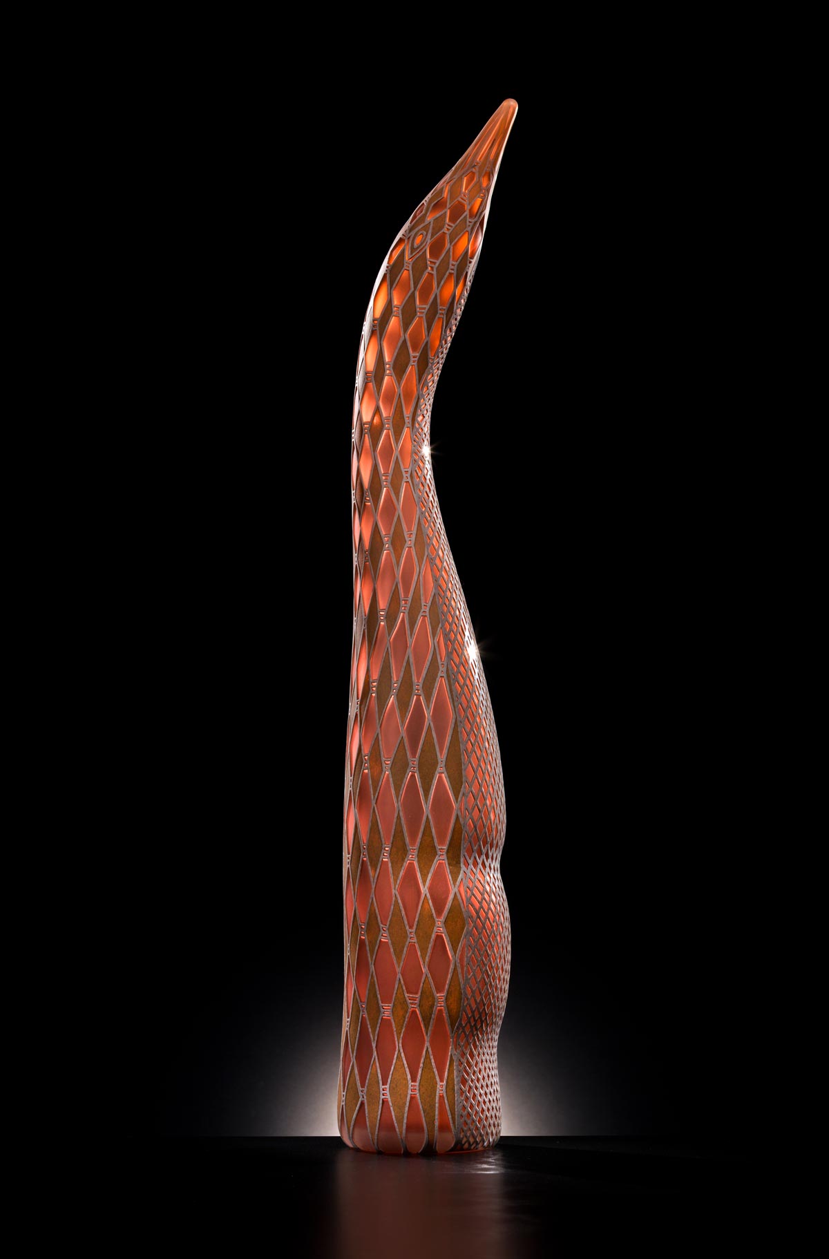 Red-orange glass sculpture of abstract form featuring reflective geometric shape