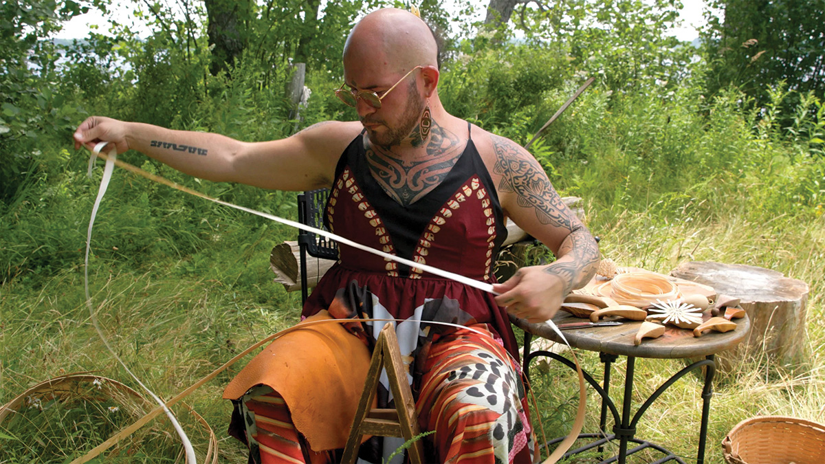 Photo of Geo Neptune seated outside, holding a long strip of wood