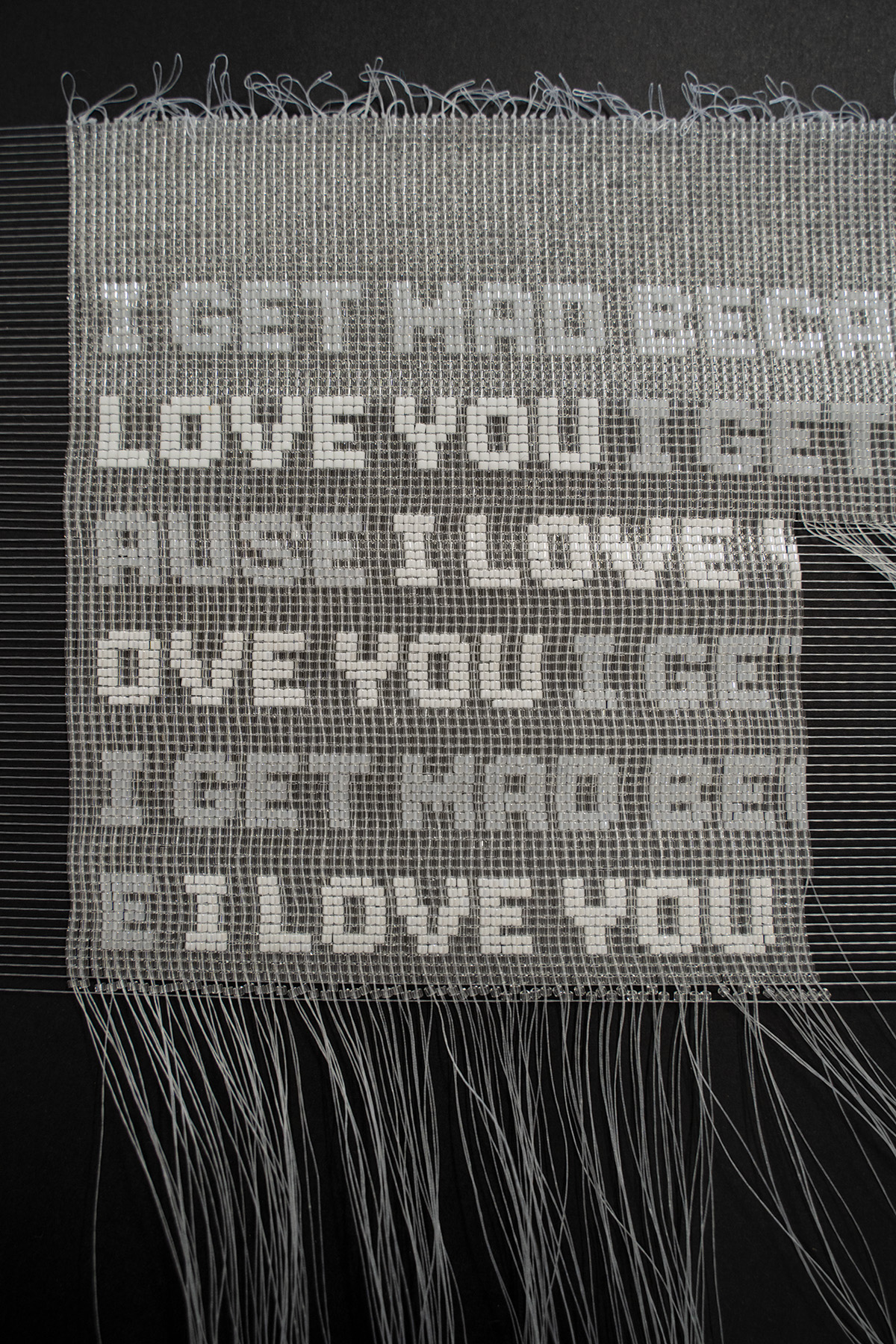A black and white beaded artwork with repeating text that reads I GET MAD BECAUSE I LOVE YOU