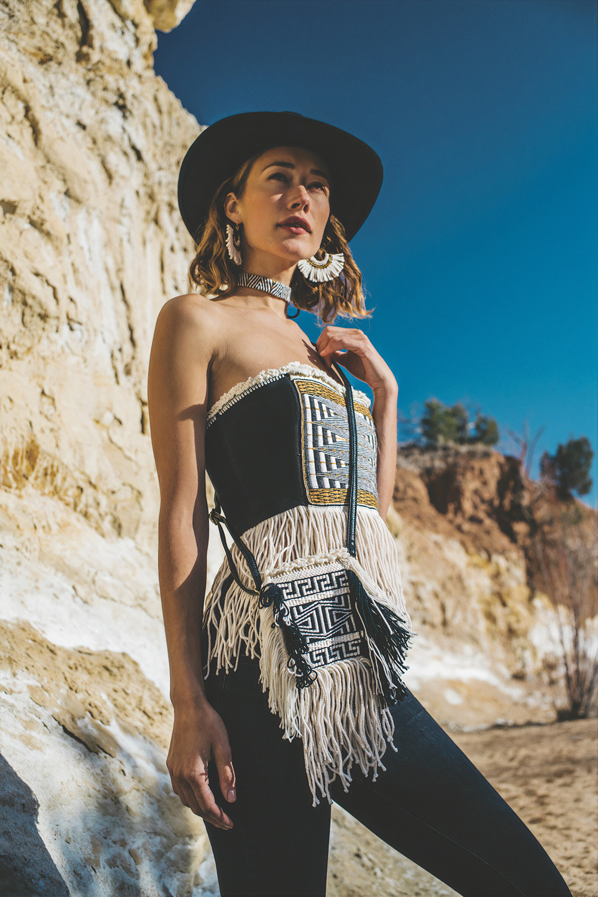 Photograph of a woman wearing a woven bodice and accessories, standing in front of a rock formation