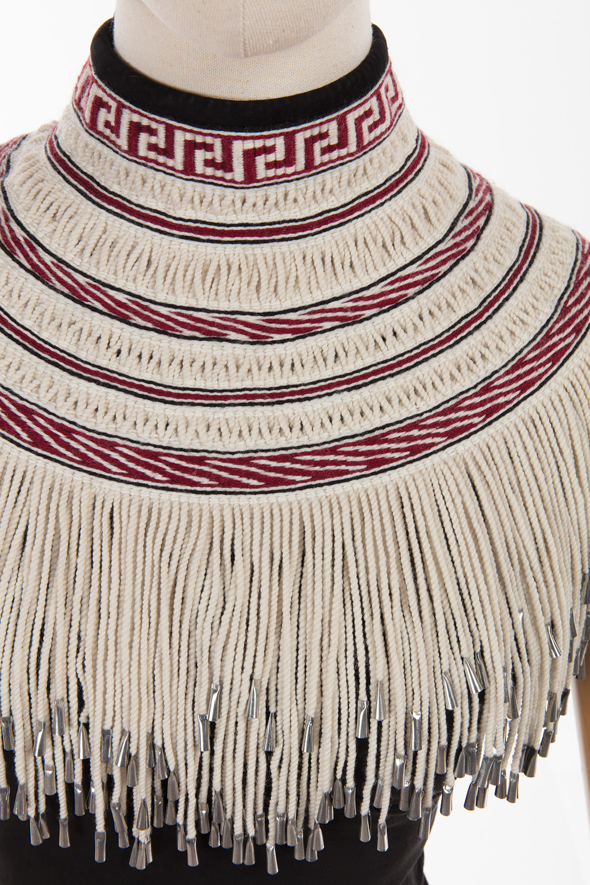 A woven garment featuring red and black designs and a white fringe, on a mannequn