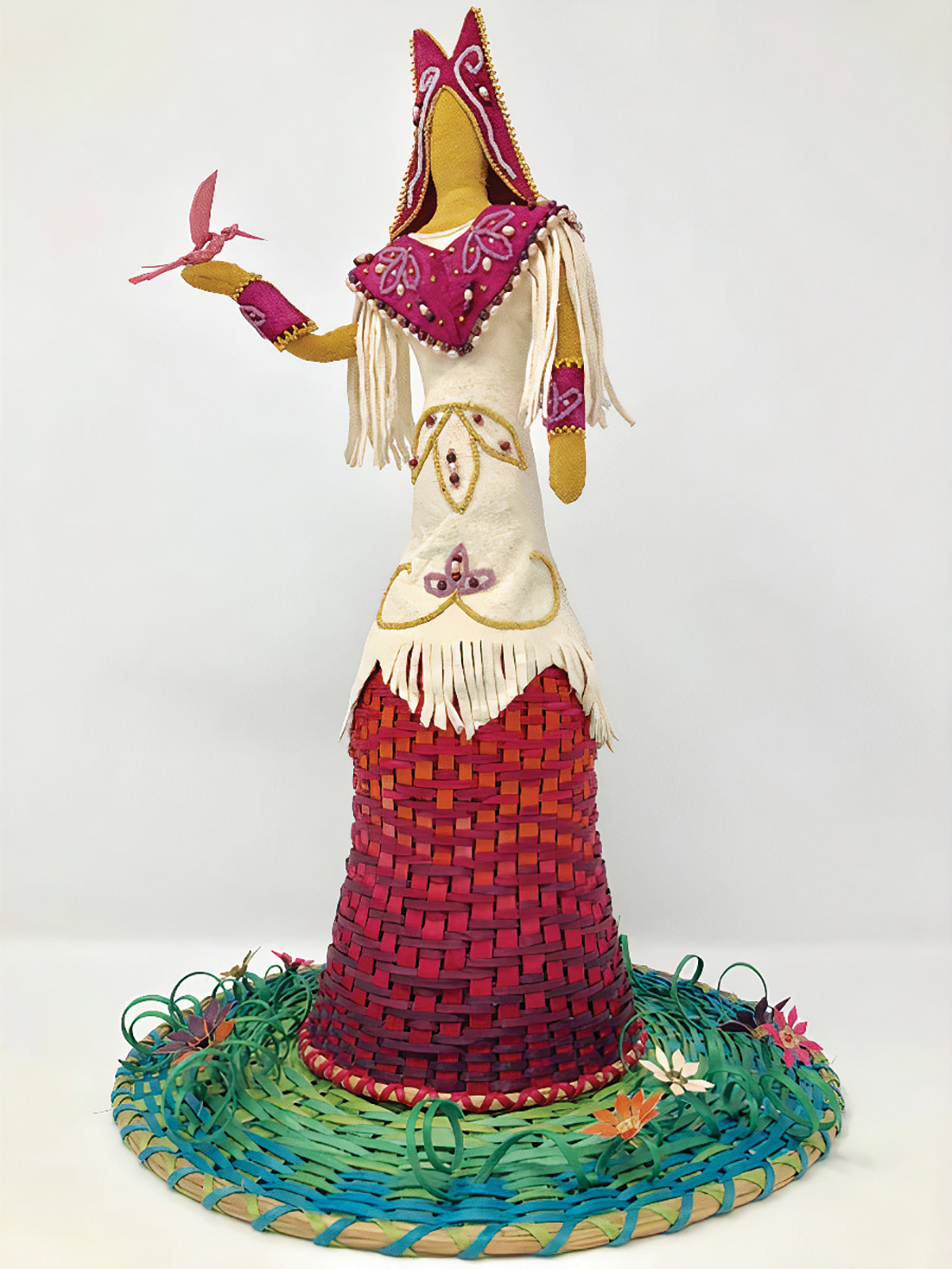 A woven artwork featuring a figure dressed in a deerskin robe, with a bird perched on one hand