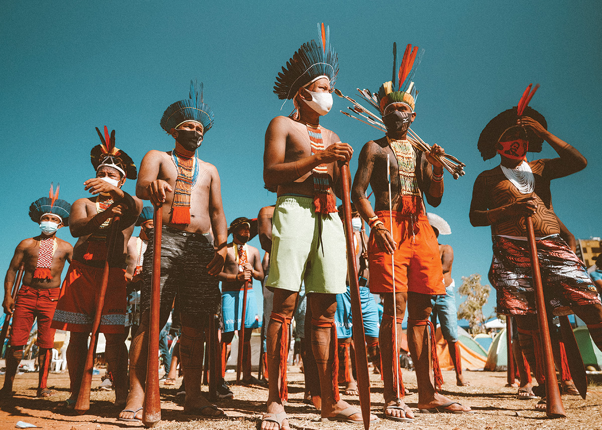A group of people dressed in regalia stand against a blue sky