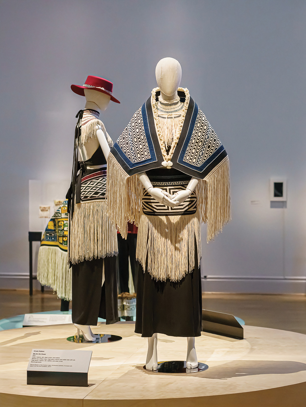 Two mannequins in a gallery wearing woven ceremonial garments