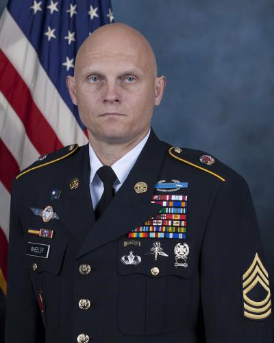 Portrait of Master Sergeant Joshua Wheeler in uniform standing in front of flag