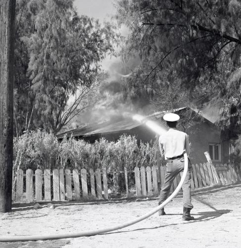 Section 14 home on fire, with fireman spraying it with water