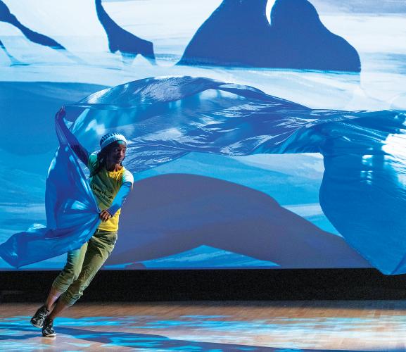 actor performing in front of projects with sheet flying behind them