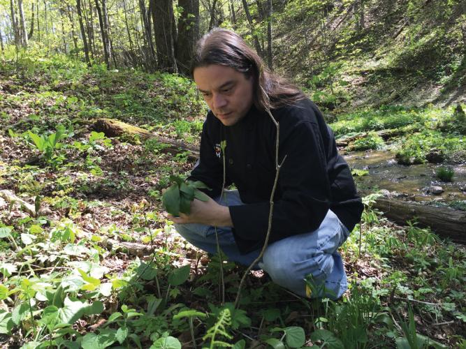 Sean Sherman crouches in the woods with a ramp in his hands