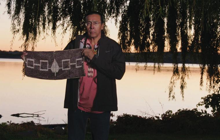 Sid Hill, the Haudenosaunee (Iroquois) Confederacy’s leader, stands near Onondaga Lake, holding the Hiawatha Belt made of wampum beads