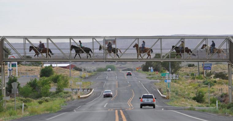 A Diné family ride their horses over Arizona State Highway 264