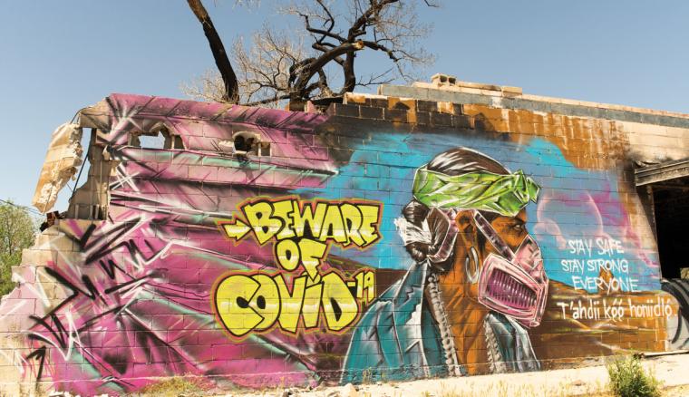 A mural depicts a man in traditional dress wearing a respirator and warns residents of COVID-19.