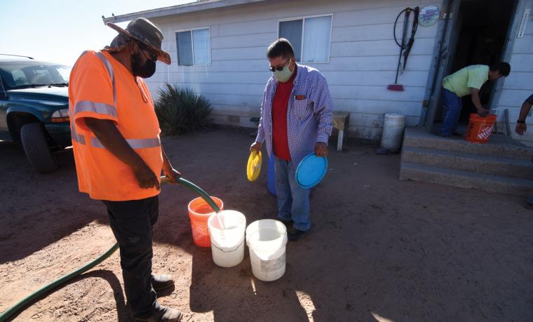 Navajo Nation Council Delegate Vince James holds bucket lids as a volunteer fills buckets with drinking water