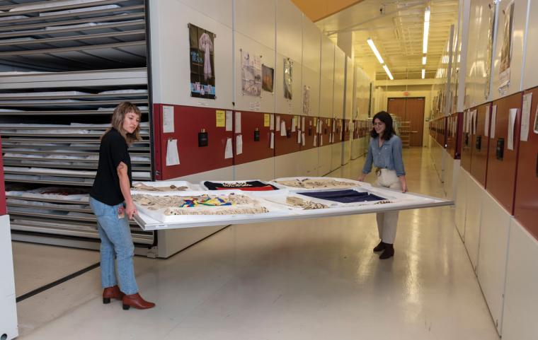 Conservators carrying a large board with clothing to the storage units that reach several feet high at the Cultural Resources Center.