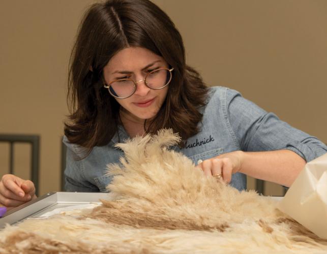 Conservator Hannah Muchnick examines a robe made of white feathers.