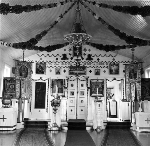 A black and white image of the interior of a church with white walls decorated with images of Jesus and saints as well as candles.