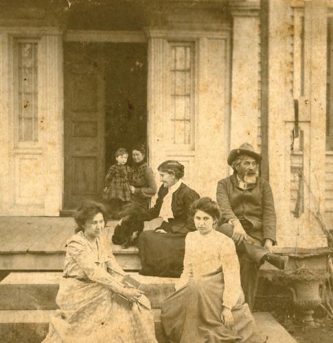 The Ross family sits on the steps to the front porch of a white house. The image is sepia-toned.