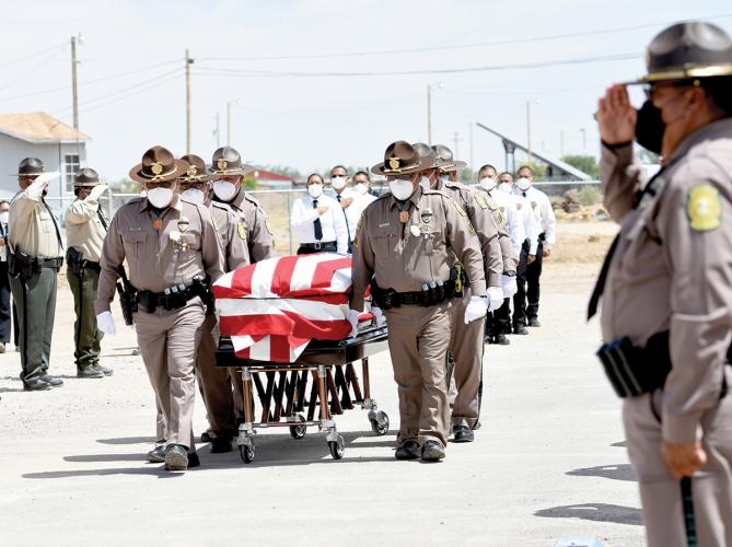 Six officers, masked and in uniform, pull a wooden casket while others around them salute or cover their hearts.
