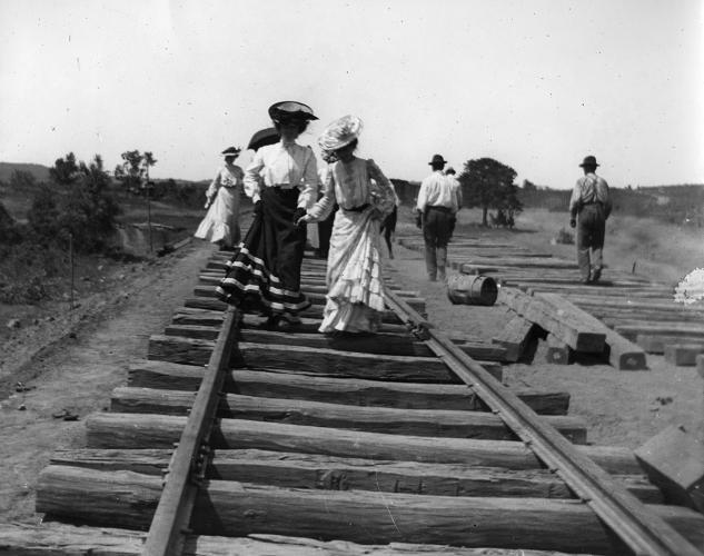Two seminary women balance on wooden train tracks. The photo is in black and white.