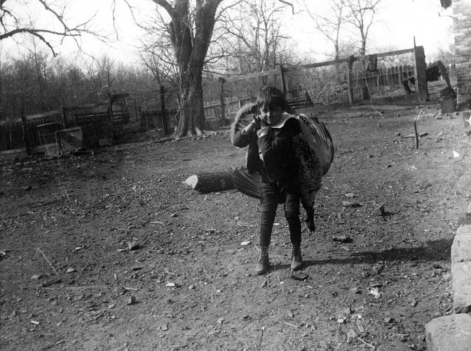A black and white photograph of a young boy with a dead turkey slung over his shoulder.