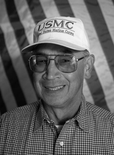 A black and white portrait of a veteran wearing a Marine trucker hat.