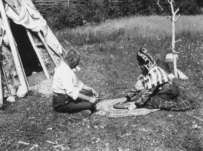 A black and white image of a man and woman sitting outside playing a dice game