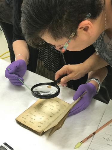 A woman uses a magnifying glass to read a Mi'kmaw hymnal