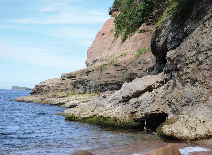 The rocky entrance to Kluskap Cave towering above the shores of a coastline in Nova Scotia