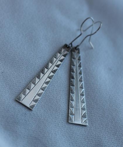 A pair of silver earrings with a traditional black chevron design.