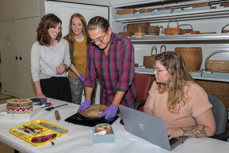 A group of people watches as dice are tossed in a wooden bowl