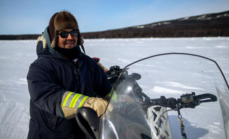 A man smiles from his snowmobile on the snowy terrain.
