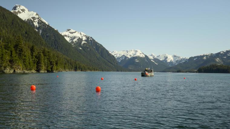 A boat moves in the water surrounded by snow-capped mountains