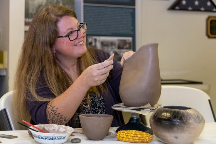 A woman with long hair uses a piece of shell to smooth a clay pot she is making