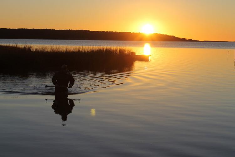 A man wades in a lake at sunset.