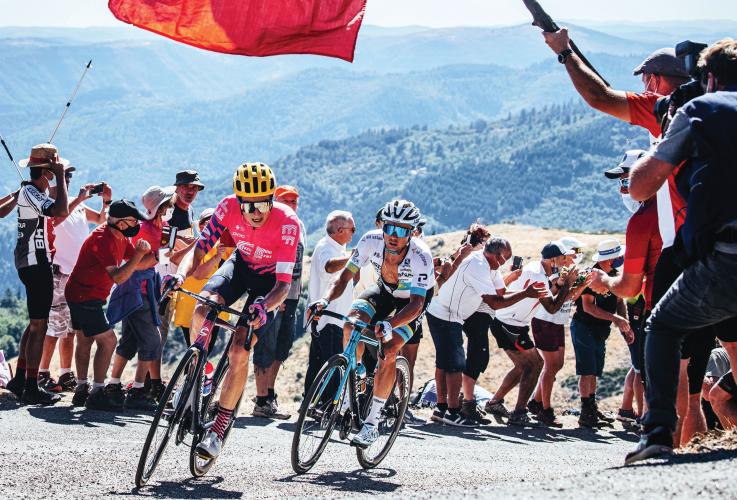 Two cyclists round a corner, surrounded by cheering onlookers