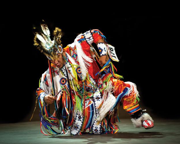 A grass dancer in an elaborately decorated outfit, captured mid-dance