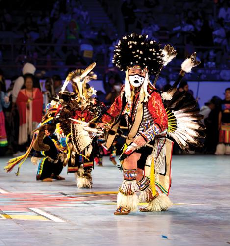 A young male dancer wearing a feather bustle and a feather headdress