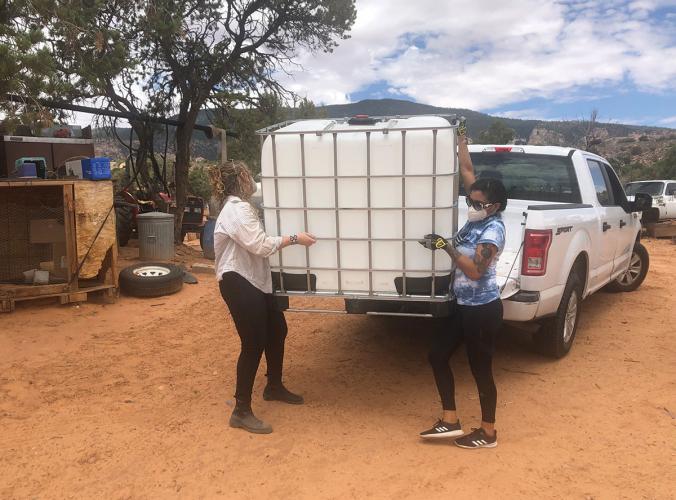 Two people unloading a water tank from a pickup truck