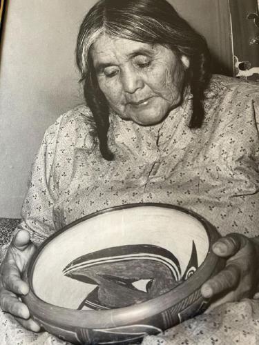 Black and white photograph of a woman holding a large shallow bowl with painted designs