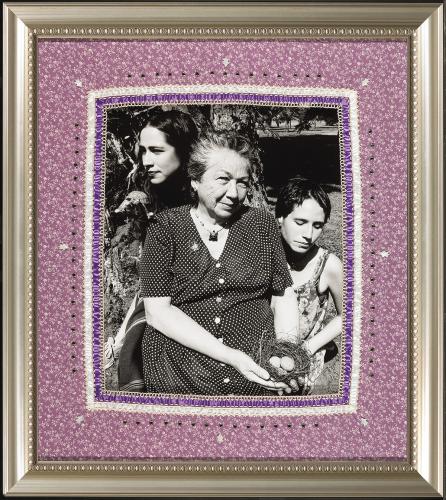 A black and white photograph of an older woman and two young women, in a metal frame. The mat is light purple and features beadwork and textile work.